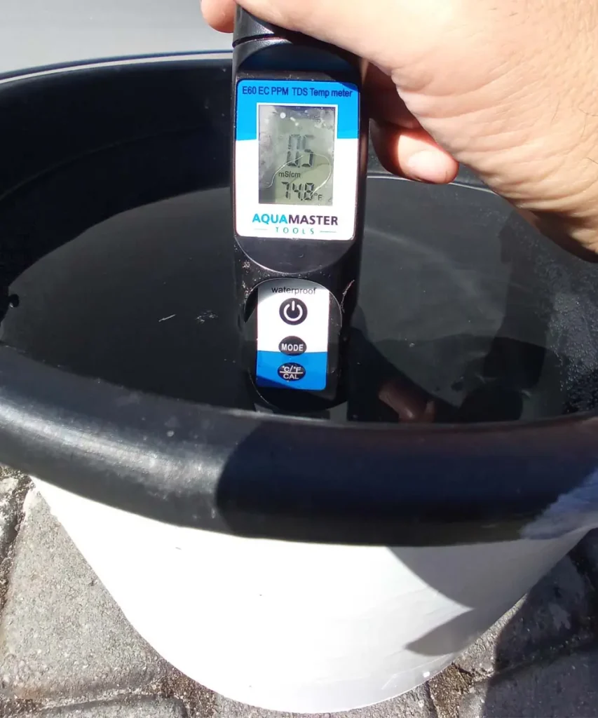 White-painted hydroponic reservoir with reflective insulation removed, showing a nutrient solution temperature of 74.8°F (23.8°C) and an EC of 0.5 mS/cm measured with a digital meter.